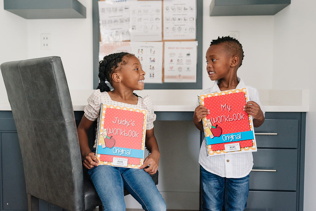 Two kindergarten age children are holding their personalized preschool workbooks